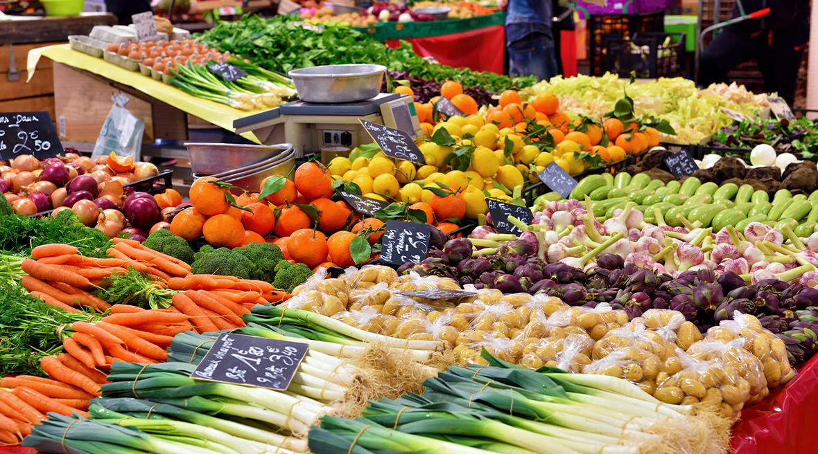 Colourful fresh fruit and vegetables laid out on a red stall at a large market